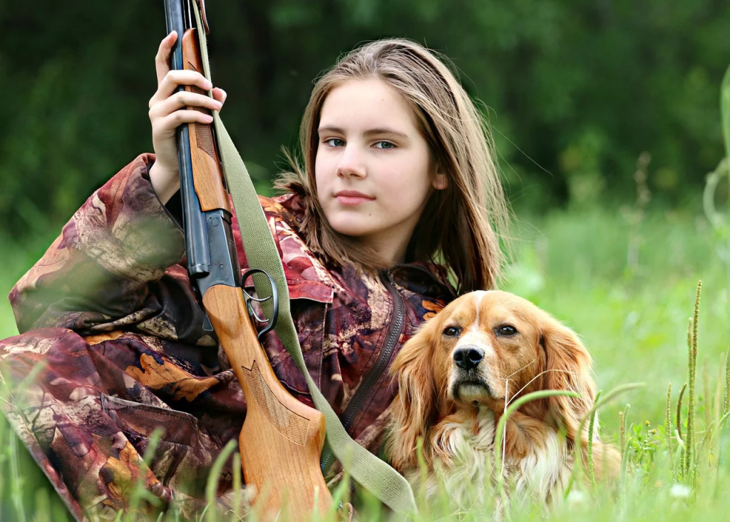 a person holding a gun and a dog in a grassy area
