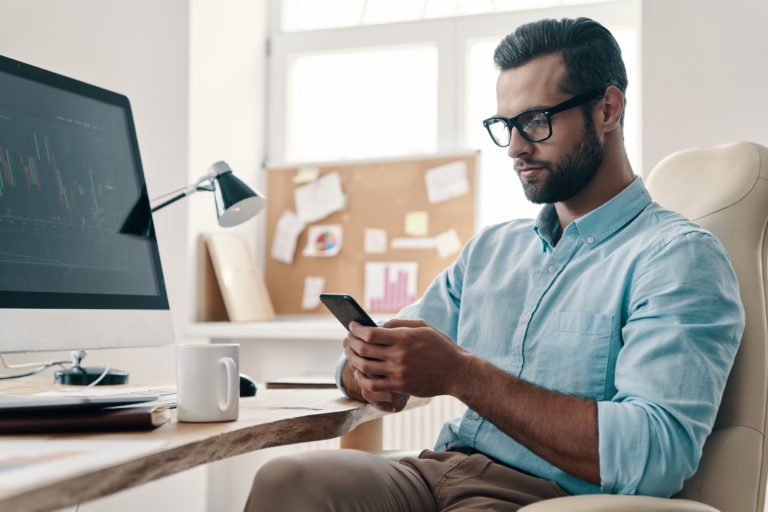 Young modern businessman using smart phone while sitting in the office