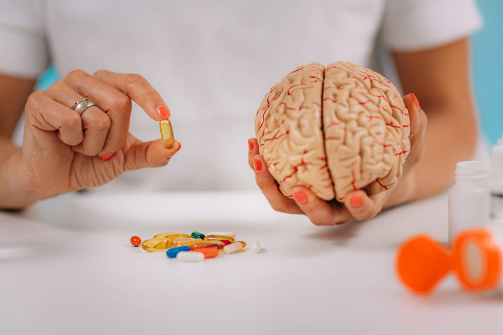 Cognitive improvement or brain supplements. Woman holding a supplement capsule and a model brain.