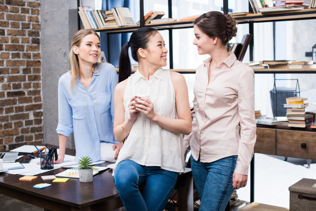 Smiling young businesswomen talking at workplace while having coffee break